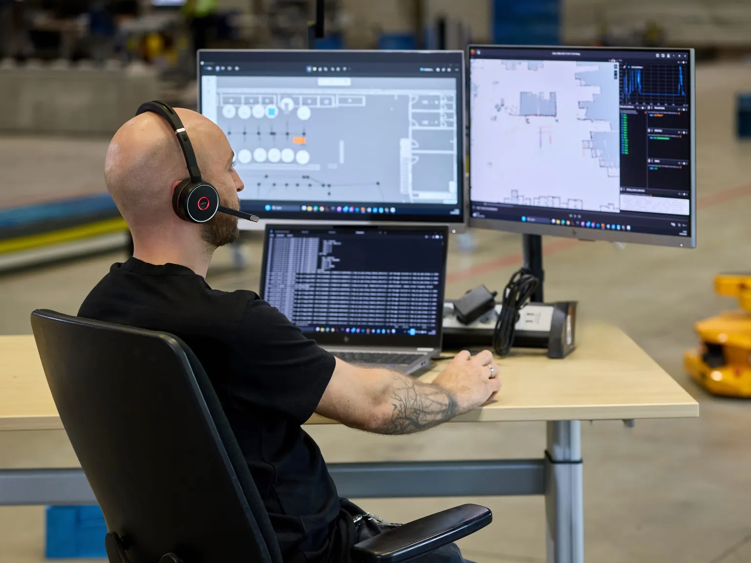 Remote-Support, Servicemitarbeiter mit Headset am Arbeitsplatz in der Halle, im Hintergrund ein AMR