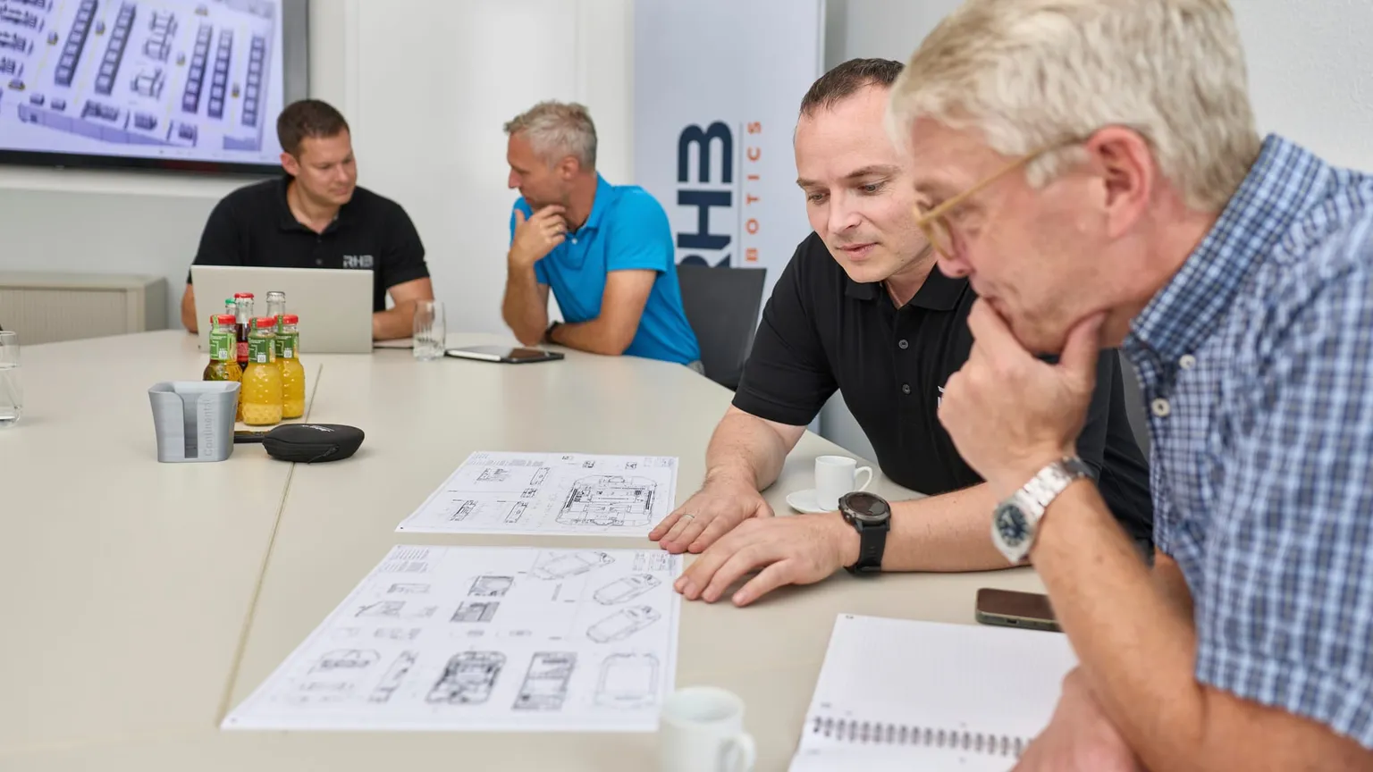 Projektbesprechung am Tisch, Kunde und RHB-Robotics prüfen gemeinsam Fahrzeugzeichnungen