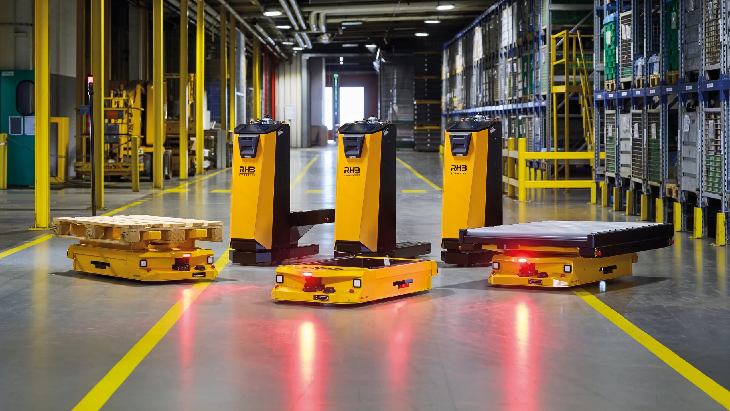 Sechs autonome Transportfahrzeuge von RHB-Robotics in einer Werkshalle: drei NXS 300 sowie IL-Fahrzeuge mit Europalette, mit Hubplattform und mit Rollenbahnaufbau