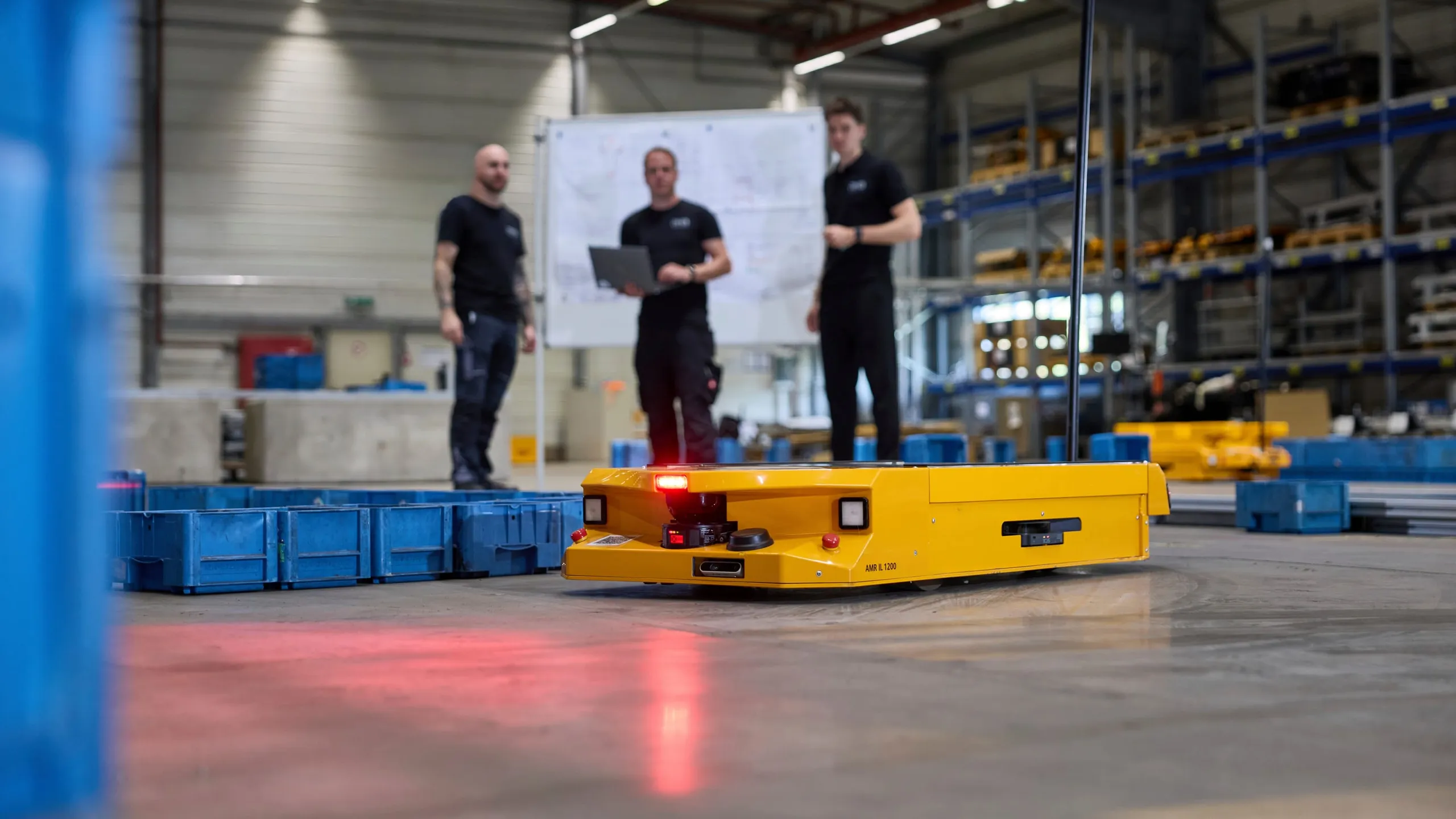 AMR IL 1200 in der Halle in Rheinböllen, im Hintergrund drei Servicetechniker mit Laptop vor einem Whiteboard